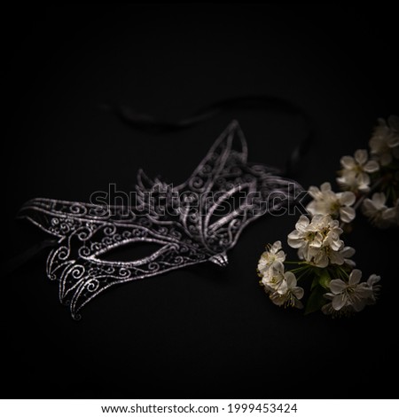 Women's openwork black mask and a sprig of flowers on a black background.