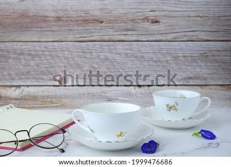 tea cup with glasses and a notebook with a pen rests on a marble table with a wooden background