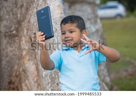 boy leaning on the tree while taking a picture with his tablet