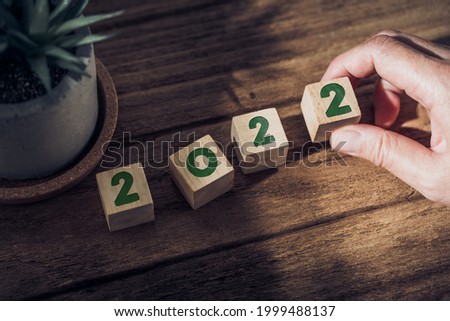 2022 happy new year with hand pick up wood block on wood table with sunlight from window.hope for new year concept