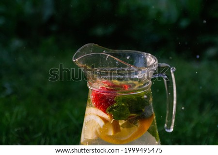 Defocus glass jug of lemonade with slice lemon and mint on natural green background with water drops. Pitcher of fresh cold summer sunny cocktail or punch. Water drops splash Copy space. Out of focus.