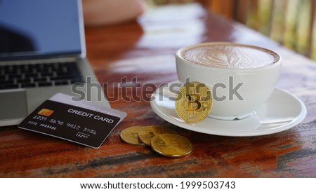 bitcoin on a coffee cup and credit cards with blurry a laptop computer on wooden table background, digital money, and business concept.