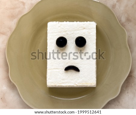 tofu block with a sad expression made of olives on a brown plate