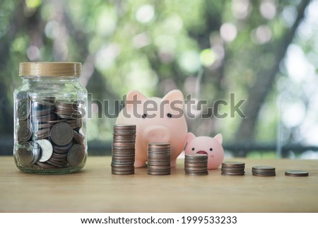 Stock of coin in glass jar and coin pile with cute piggy bank on wood table. Finance, saving money. Business to success and saving for retirement concept