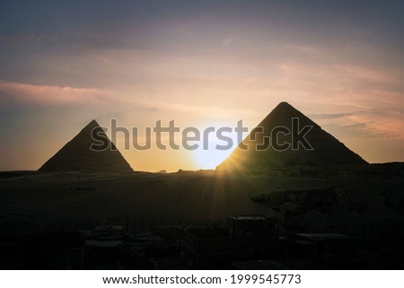 Archaeological complex of the Great Egyptian Pyramids is located on Giza plateau. Pyramids of Chephren Khafra and Cheops Khufu in the night light at sunset. sun sets behind the pyramid. Cairo, Egypt.