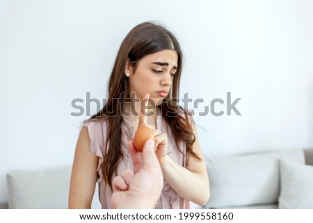 Selective focus of a beautiful young women  refusing to eat eggs.  Young beautiful woman holding fresh egg at home with open hand doing stop sign with serious and confident expression. 