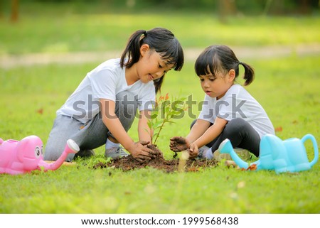 Two cute little girl asia planting young tree on black soil in the park.Which increases the development and enhances learning skills as save world new life,environmental conservation concept.