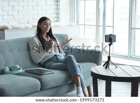 A young blogger streaming online in a social network and communicates with her subscribers, recording video blog podcast on smart phone sitting at home, chatting on a video call with friends