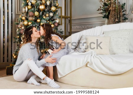 Cheerful mom and her cute daughter girl exchanging gifts on Merry Christmas and Happy New Year. Mother and little child having fun near Christmas tree indoors. Lovely family with presents in room