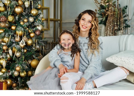 Cheerful mom and her cute daughter girl exchanging gifts on Merry Christmas and Happy New Year. Mother and little child having fun near Christmas tree indoors. Lovely family with presents in room