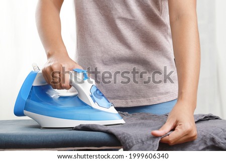 Woman ironing clothes on ironing board in laundry room at home, housework, wife
