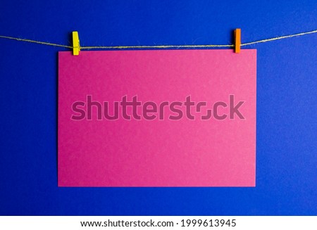 a red sheet of paper is suspended on a rope on a blue background. cardboard is held on a yellow and orange pin