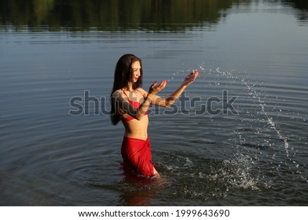 Beautiful brunette girl in red bikini playing with water in the lake