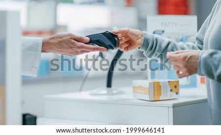 Pharmacy Drugstore Checkout Cashier Counter: Pharmacist and a Customer Using Contactless Credit Card with Payment Terminal to Buy Prescription Medicine, Health Care Goods. Close-up Focus on Hands Royalty-Free Stock Photo #1999646141