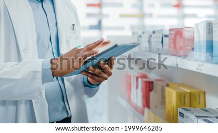 Pharmacy: Portrait of Professional Black Pharmacist Uses Digital Tablet Computer, Checks Inventory of Medicine, Drugs, Vitamins, Health Care Products. Druggist in Drugstore Store. Focus on Hands Royalty-Free Stock Photo #1999646285