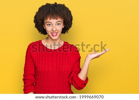 Young hispanic girl wearing casual clothes smiling cheerful presenting and pointing with palm of hand looking at the camera. 