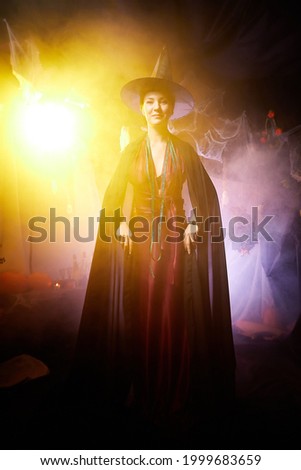 Young brunette witch with clouds of smoke behind her in Halloween location in studio. Witchcraft and wizardry in carnival.