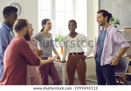 Diverse group of happy cheerful friends meet and have fun together. Bunch of positive young multiracial people standing in office or living-room, talking, sharing news and funny stories and laughing Royalty-Free Stock Photo #1999696112