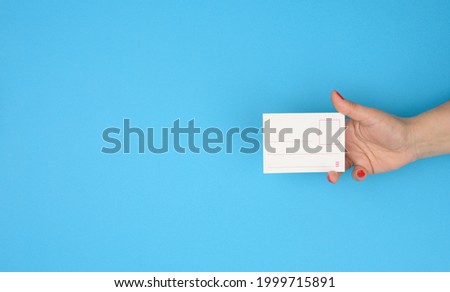 female hand holding paper blank badge insert on blue background, copy space