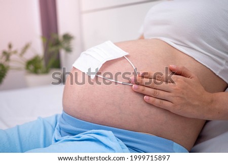 A pregnant woman at 28 weeks wears a mask on her stomach to prevent viruses and pollen or PM2.5 dust.