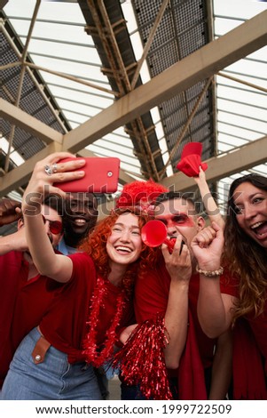 Vertical photo of a group of people taking a smiling selfie while cheering for their sports team from a stadium. Cheerful fans take a cell phone photo while celebrating at the stadium.