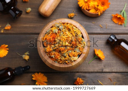 Dry calendula flowers and bottles of essential oil on wooden table, flat lay