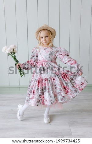 Girl in a dress Blond child with blue eyes in a hat holding white flowers carnation in his hands creative style of clothing