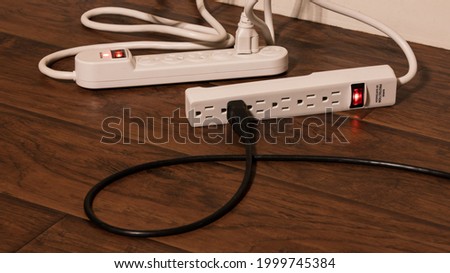 A black power cord plugged into a surge protector which is plugged into another extension cord. Known as daisy stripping, this usage of power strips is a fire hazard and is highly dangerous. Royalty-Free Stock Photo #1999745384
