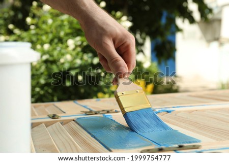 Man painting wooden surface with blue dye outdoors, closeup