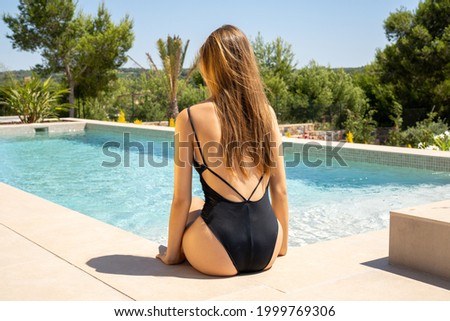 Young woman from back sits on pool