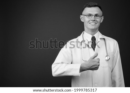Studio shot of young man doctor wearing eyeglasses against gray background in black and white