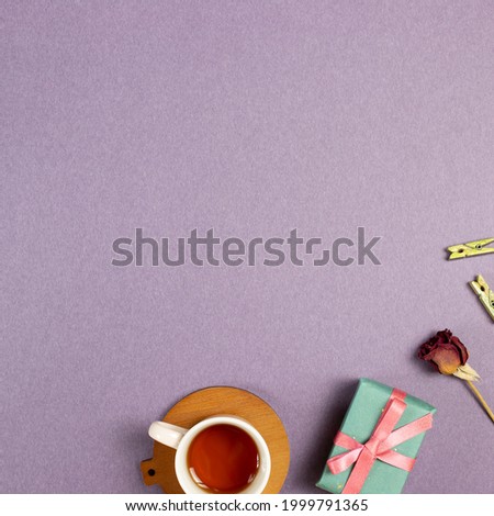 Gift box, cup of tea, wooden clip, dry rose flower on purple background. flat lay, top view, copy space