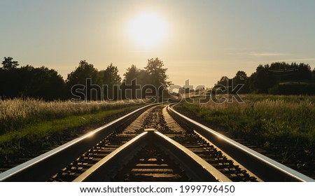 A beautiful summer sunset over the empty railroad tracks running through colorful meadows. Scenery. Horizontal photo.