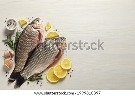 Fresh raw crucian carps and ingredients on light wooden table, flat lay with space for text. River fish Royalty-Free Stock Photo #1999810397