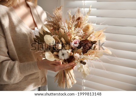 Woman holding beautiful dried flower bouquet near window at home, closeup Royalty-Free Stock Photo #1999813148