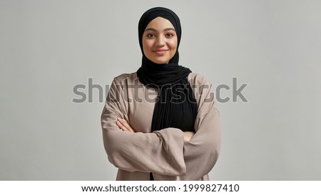 Portrait of smiling young arabian girl in black hijab looking at camera on light background, widescreen. Beautiful muslim lady Royalty-Free Stock Photo #1999827410