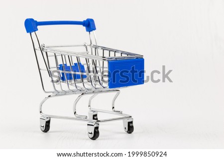 empty metal shiny grocery cart on wheels on white wooden table background