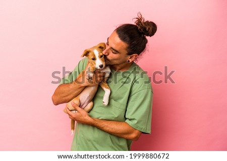 Young caucasian man holding his puppy isolated on pink background
