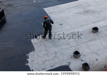 Waterproofing coating. A worker applies bitumen mastic to the foundation. Roofer cover the waterproofing primer on the roof, modified with polymer bitumen, with a roller brush. Royalty-Free Stock Photo #1999898915