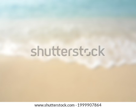 blur the seaside beach background with light brown sand tiny foamy white waves and light blue water use as a backdrop