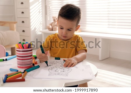 Cute child coloring drawing at table in room