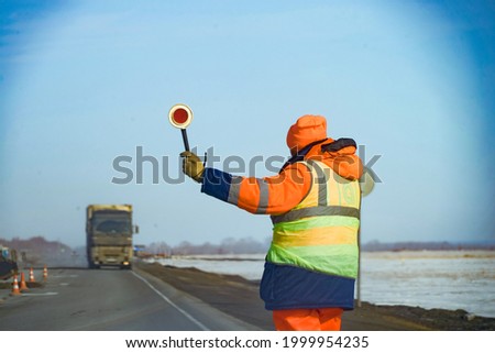 Close-up and rear view of a male road construction worker holding a stop stick, wearing high visibility protective clothing, road work management