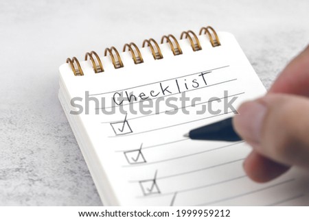 Hand with black pen marking on checklist box in a spiral notepad.