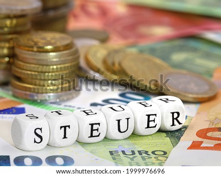 german word for Tax, STEUER, written with letter cubes on euro banknotes and coins background, concept image of increasing tax or paying taxes. Royalty-Free Stock Photo #1999976696