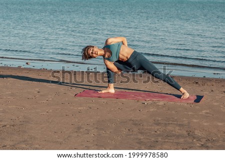 a young attractive woman, of Asian appearance, practicing yoga, performs a stretching exercise, on the beach. the exercise utthita baddha PARSHVAKONASANA