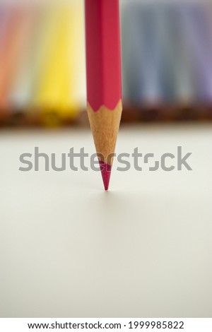 red pencil is directed vertically with the point downward against a white background and is positioned against a blurred background of colored pencils. For design. Cover.