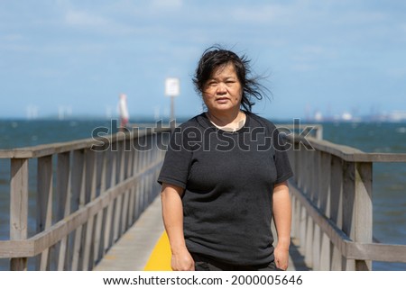 An Asian middle aged woman on a jetty with a blue ocean and sky in the background. Picture from Scania county, Sweden