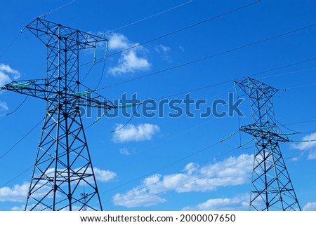 Two high voltage transmission towers against a background of blue sky and cumulus clouds. Part of a general industrial network. The pylons are located on the right and left.