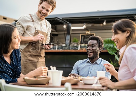 Food truck owner taking customers orders with mobile device - Happy multiracial people having a meal outdoor Royalty-Free Stock Photo #2000014670