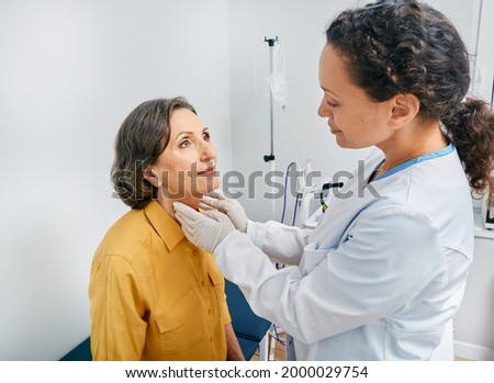 Doctor palpates of mature woman's neck for diagnostics of thyroid diseases and hypothyroidism at medical clinic. Thyroid treatment Royalty-Free Stock Photo #2000029754